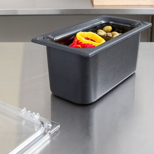 A Carlisle Coldmaster 1/3 size divided black food pan with vegetables and yellow and red peppers.