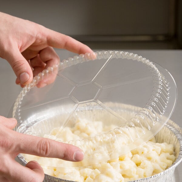 A person placing a Choice plastic dome lid on a plastic container of food.