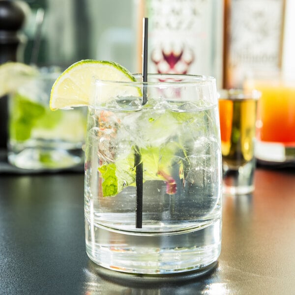 A Libbey rocks glass with clear liquid, ice, a straw, and a lime wedge.