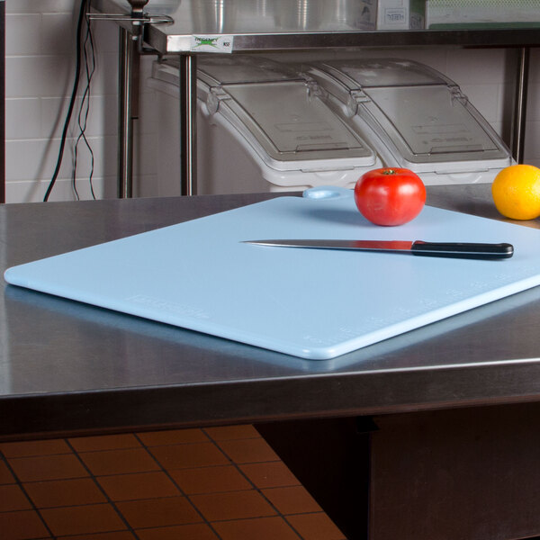 A blue San Jamar Cut-N-Carry cutting board with a knife and tomato on a counter.