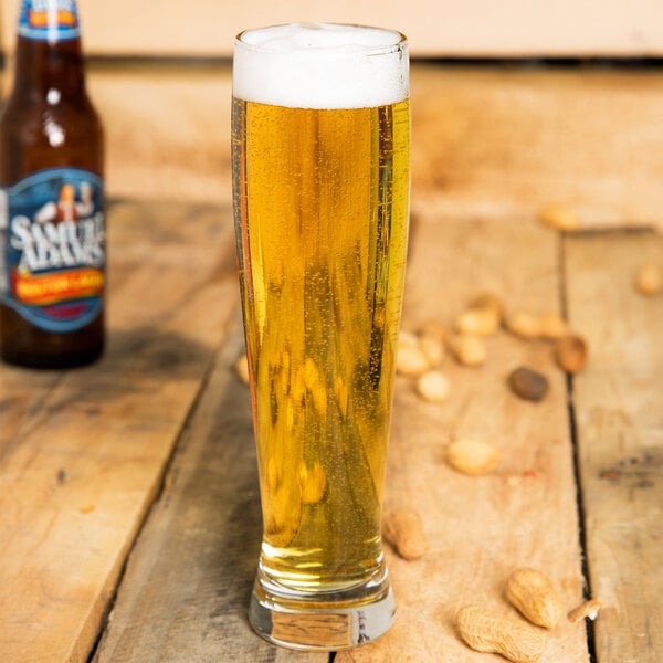 A close up of a Libbey Altitude Pilsner glass of beer with peanuts on a wooden table.