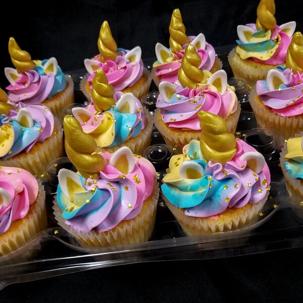 A white fluted baking cup with a cupcake decorated with a unicorn horn on a bakery display tray.