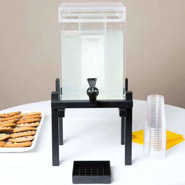 A black Cal-Mil plastic beverage dispenser on a table with cookies and crackers.