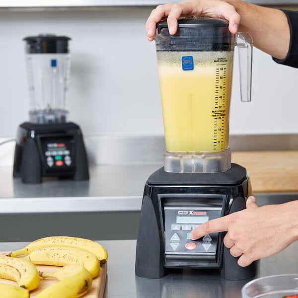 A person using a Waring commercial blender to blend a yellow smoothie.