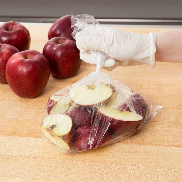 A gloved hand placing red apples in an Inteplast Group plastic food bag.