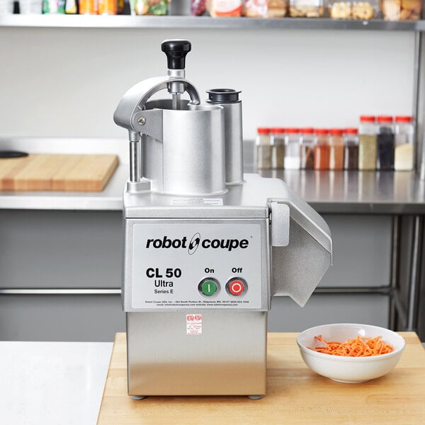 A Robot Coupe CL50 Ultra food processor on a counter with a bowl of shredded carrots.