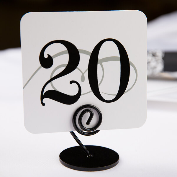 A white square table card holder with black numbers on it holding a number card.
