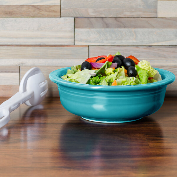 A Fiesta turquoise serving bowl filled with salad on a table with a spoon.