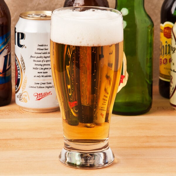 A Libbey pub glass filled with beer on a table with bottles.