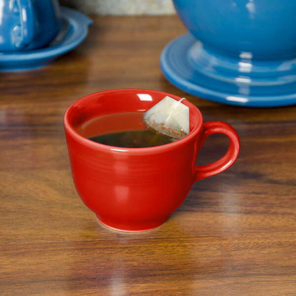 A red Fiesta china cup with liquid and a tea bag in it on a table.