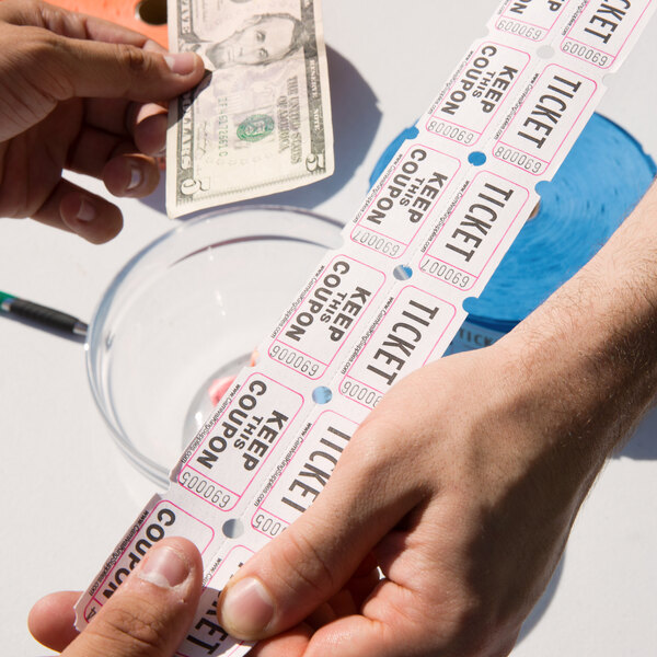 A pair of hands holding Carnival King customizable raffle tickets over a bowl of money.