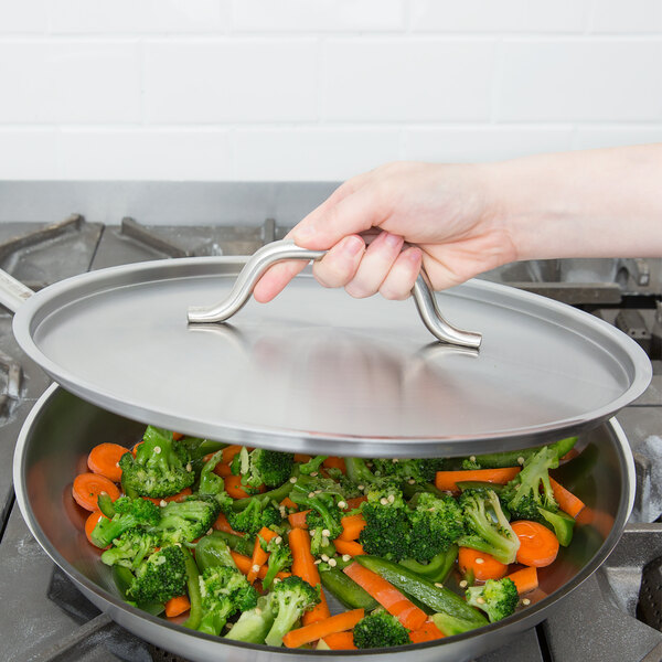 A hand using a Vollrath Optio cover to hold a lid over a pan of vegetables.
