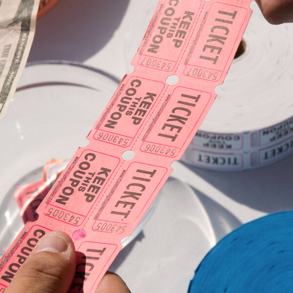 A hand holding a roll of pink Carnival King raffle tickets.