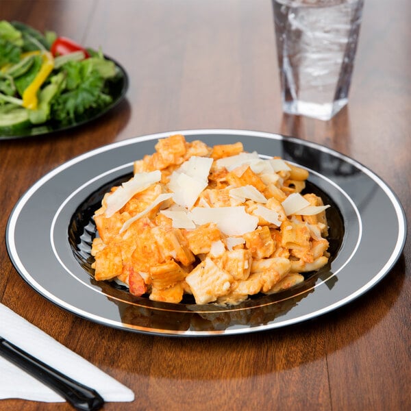 A Fineline black plastic plate with silver bands holding pasta, chicken, and vegetables.