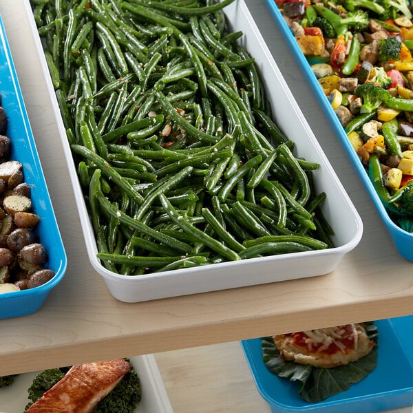 A white fiberglass market pan filled with green beans and other vegetables on a table.