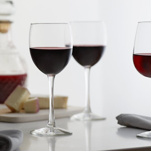 Three Libbey Vina tall wine glasses filled with red wine on a table.