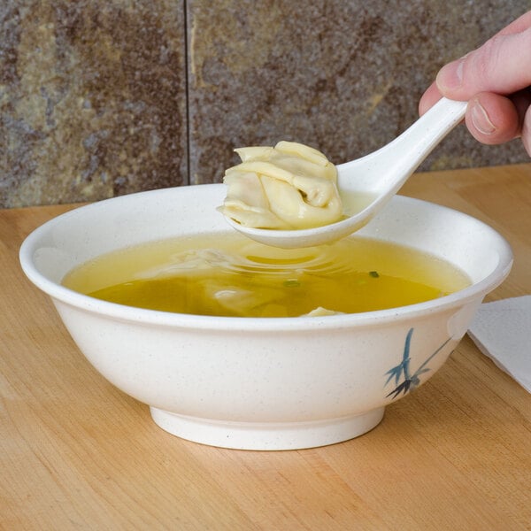 A Thunder Group Blue Bamboo melamine wonton soup spoon holding soup over a bowl.