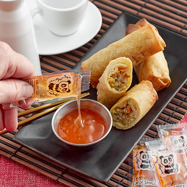 A hand pouring Duck Sauce onto a plate of spring rolls.