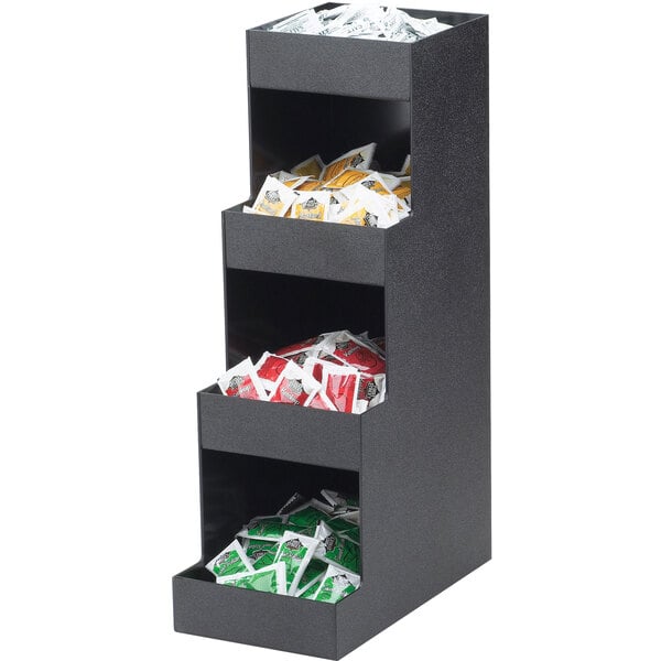 A black four tier Cal-Mil condiment organizer on a counter with compartments holding packets.