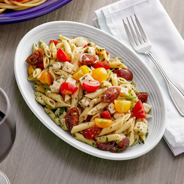 A Tuxton white oval china coupe platter with pasta salad, tomatoes, and olives.