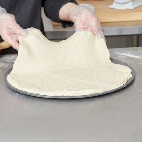 A person holding a pizza dough on a plate.