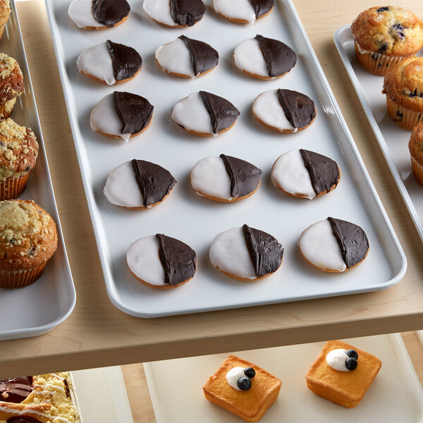 A white Cambro market tray with cookies, muffins, and pastries on a bakery display counter.