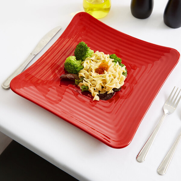 A red square GET Melamine plate with noodles and broccoli on a table.