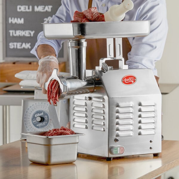 A man using an Avantco meat grinder on a counter in a butcher shop.