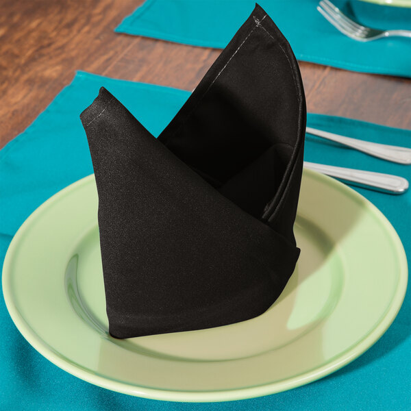 A black Intedge polycotton blend napkin folded on a plate.