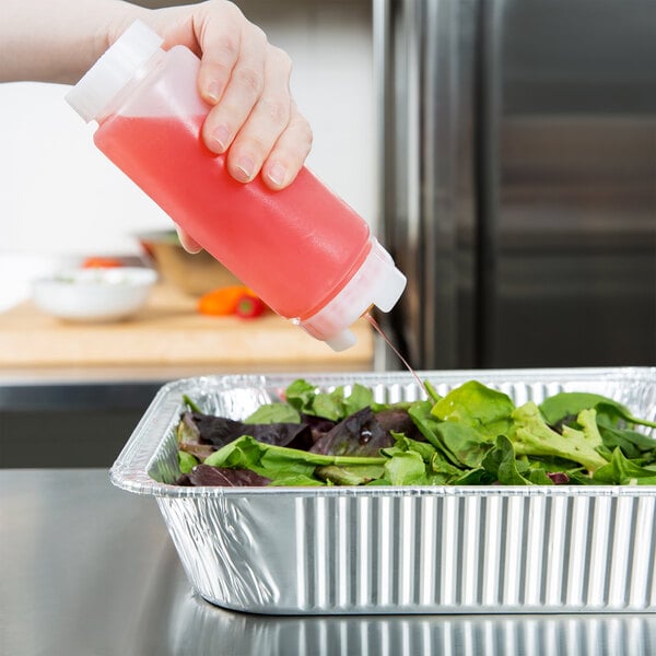 A hand using a FIFO Innovations squeeze bottle to pour pink liquid onto a salad.