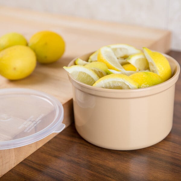 A Carlisle beige plastic crock with a lid on a counter with lemons inside.