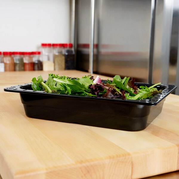 A black melamine food pan filled with lettuce on a counter.