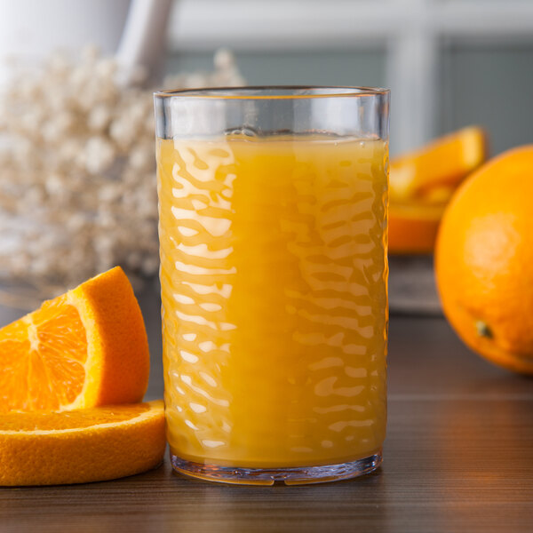 A Carlisle clear plastic tumbler filled with orange juice with a slice of orange on the rim.