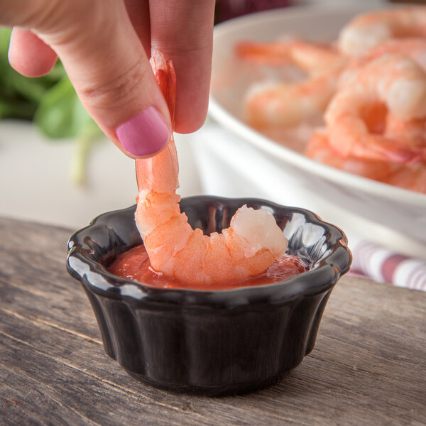 A hand holding a shrimp in a bowl of sauce.