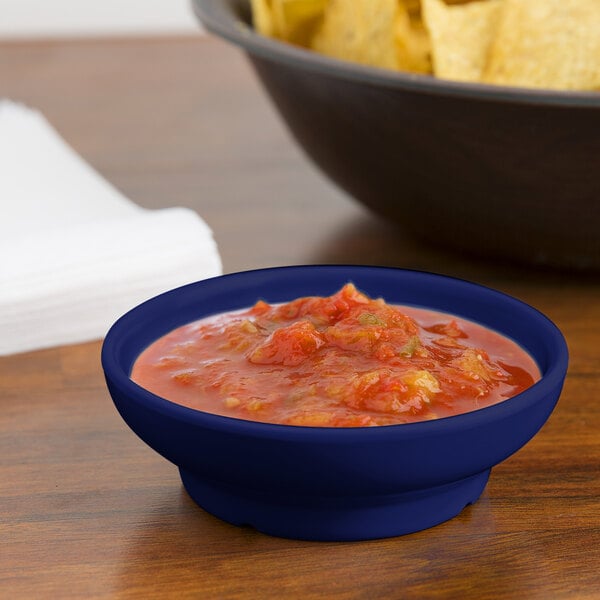 A cobalt blue GET melamine salsa dish filled with salsa next to a bowl of chips on a table.
