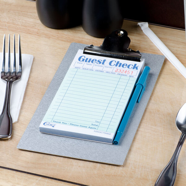 A Menu Solutions brushed aluminum clipboard with a guest check on a table.