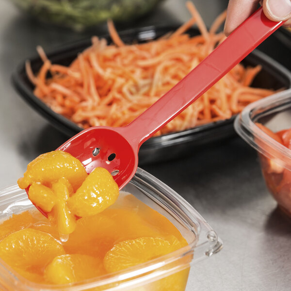 A person using a red Thunder Group polycarbonate perforated salad bar spoon to serve oranges in a container.