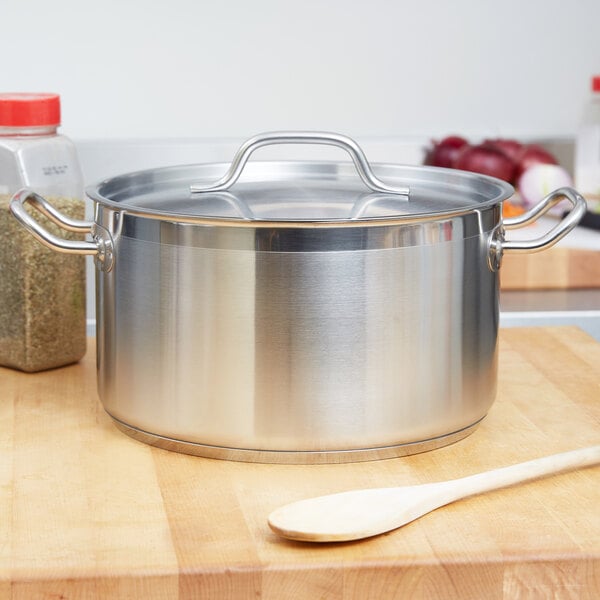 A silver Vollrath sauce pot with a metal handle on a wooden cutting board.