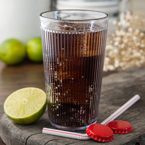 A Carlisle clear plastic tumbler filled with soda and ice with a lime and straw.