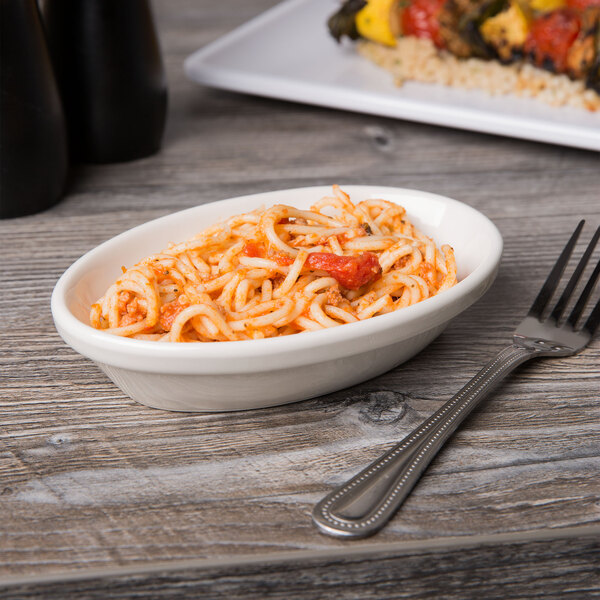 A Tuxton eggshell oval baker filled with spaghetti and tomato sauce with a fork on the table.