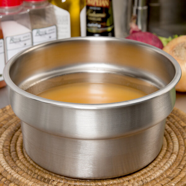 A Vollrath stainless steel vegetable inset with brown liquid inside.