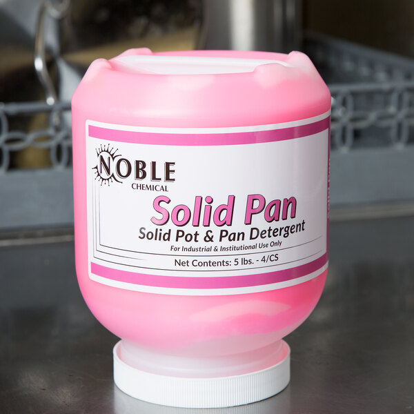 A pink plastic container of Noble Chemical Concentrated Solid Pan Detergent on a counter.