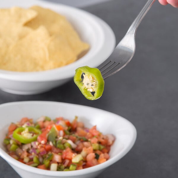 A fork with a slice of whole jalapeno pepper on it next to a bowl of chips.