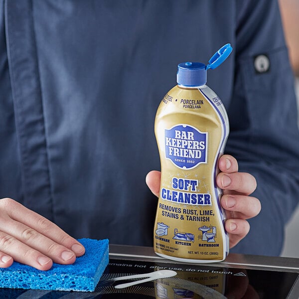 A person holding a bottle of Bar Keepers Friend All Purpose Soft Cleanser.