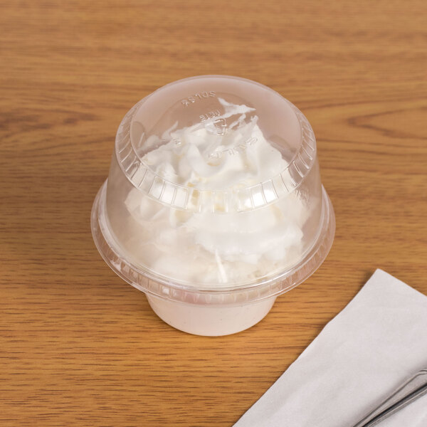 A Solo clear plastic sundae lid filled with whipped cream on a table.