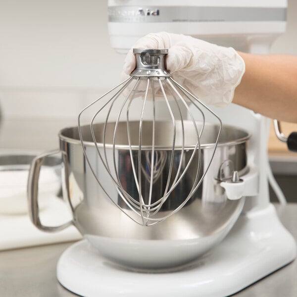 A person using a KitchenAid wire whip attachment on a stand mixer.