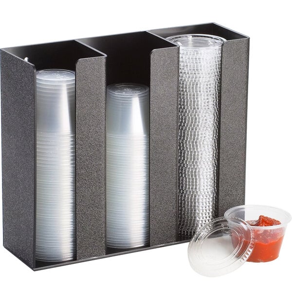 A black Cal-Mil countertop organizer with 3 sections holding plastic cups and a container with a lid.
