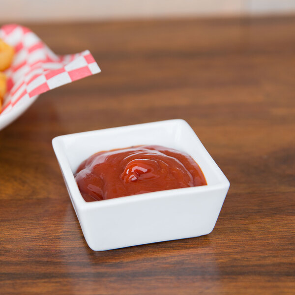A CAC square china bowl filled with ketchup and french fries on a table.