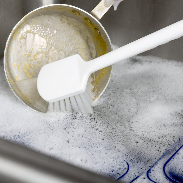 A Wells fry pot cleaning brush in soapy water on a counter.