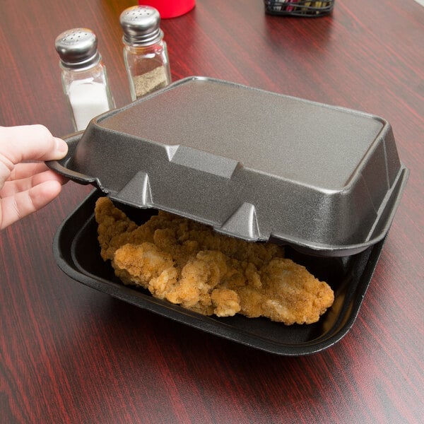 A hand holding a Genpak black foam container with food in it.